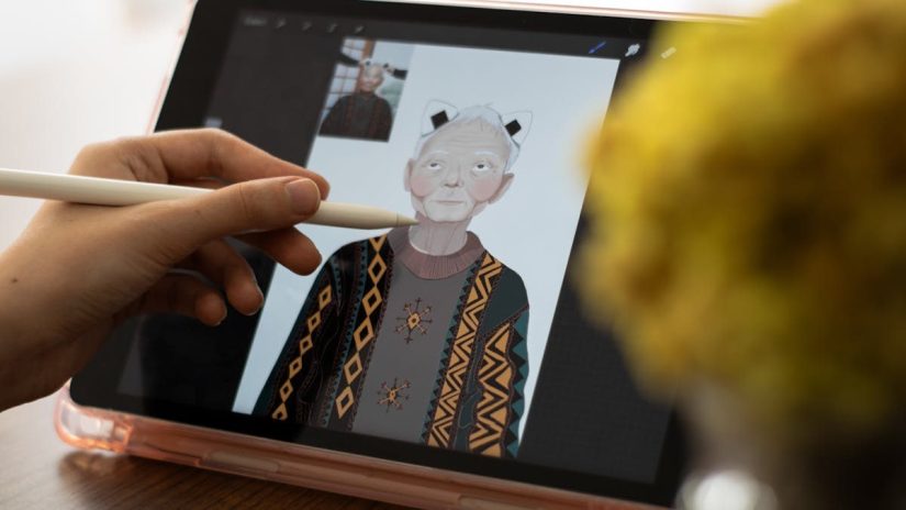 Close-up of hands using a tablet and stylus for digital art creation, depicting an elderly character.