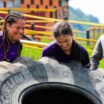 Two women and a man engage in an outdoor fitness session flipping a large tire.